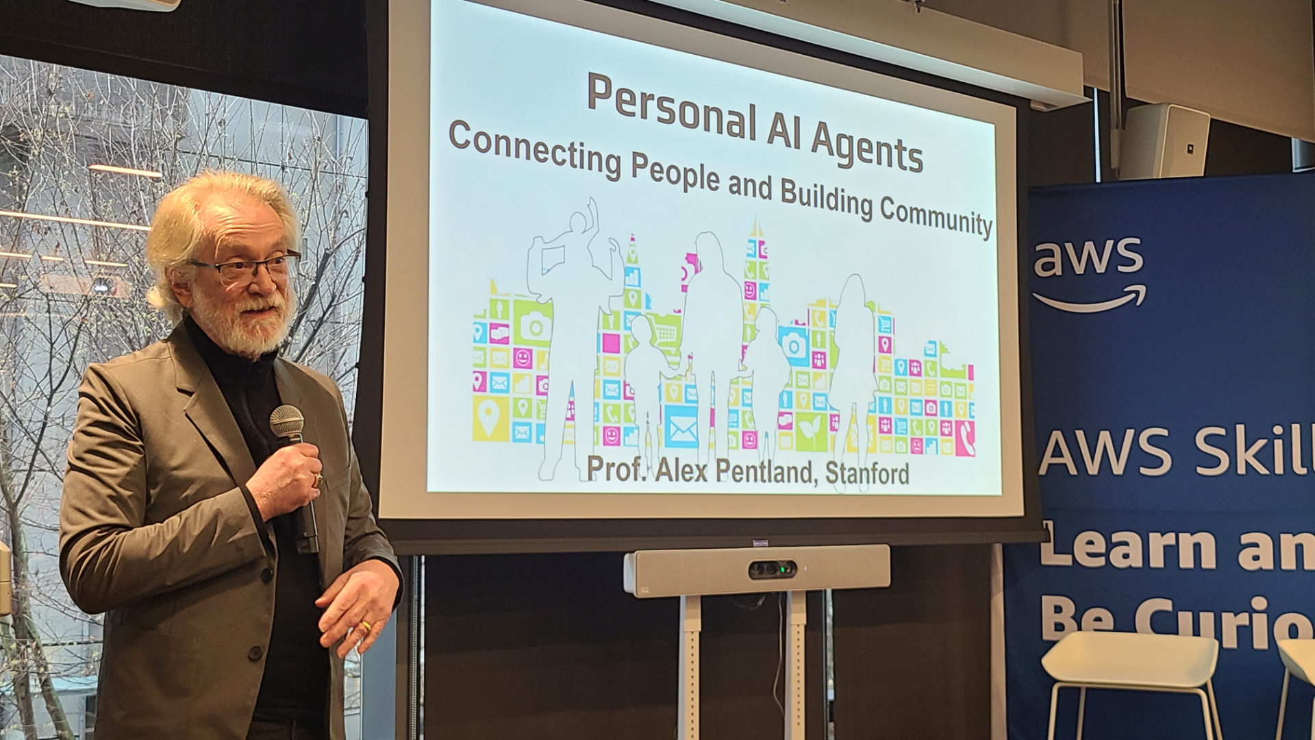 Sandy Pentland speaking in front of a slide titled "Personal AI Agents: Connecting People and Building Community."